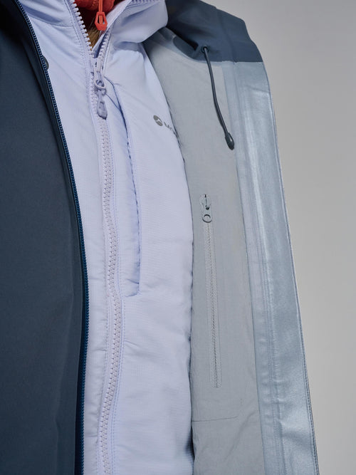 Close-up of a technical outdoor jacket showing a light blue inner layer under a gray and navy outer shell with a drawstring hood.