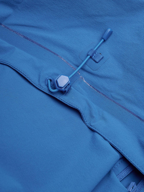 Close-up of a blue waterproof jacket detail, showing a drawcord closure with a plastic toggle and hook.