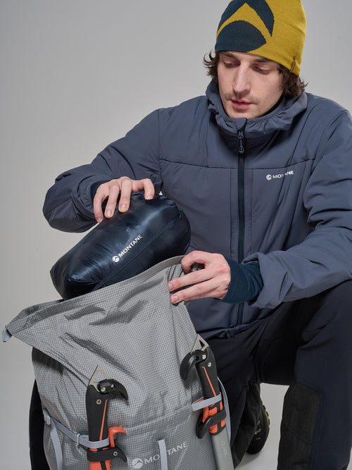 Person in outdoor gear with a backpack and insulated bag on a gray background